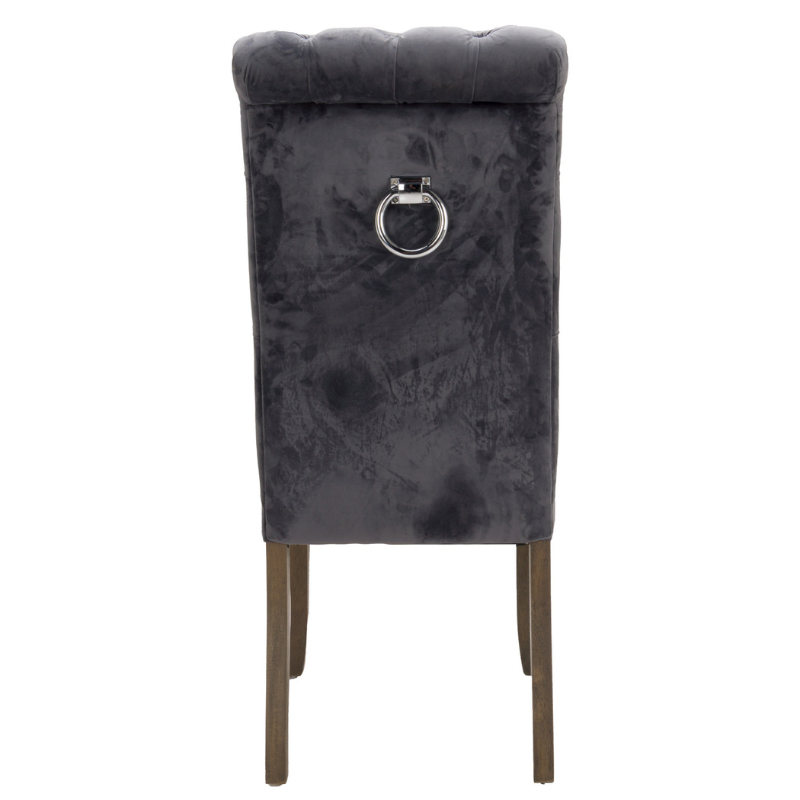 This is the Knightsbridge Roll Top Dining Chair. A sumptuous button pressed velvet chair in a timeless great colour with roll-top detail and silver ring pull that will add elegance and class to a variety of interiors. Built from a rubberwood frame, known for its dense grain and strength, it is a sturdy piece, ready for everyday use. All upholstered items have passed UK fire safety regulations with cigarette and match test certificates.